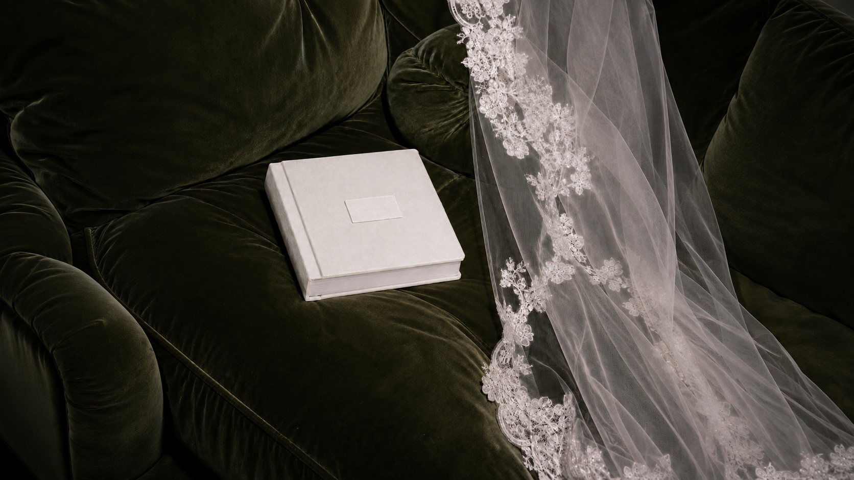 Suede album and lace veil styled on a green velvet sofa